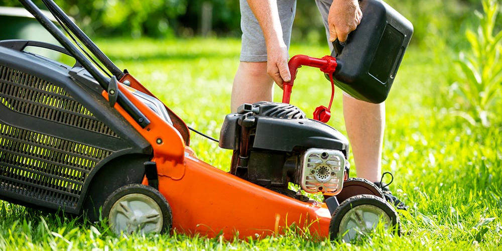 Person refueling a lawn mower on green grass