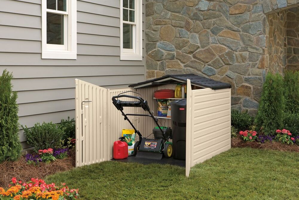 Small outdoor storage shed next to a house, holding a lawn mower and gardening supplies.
