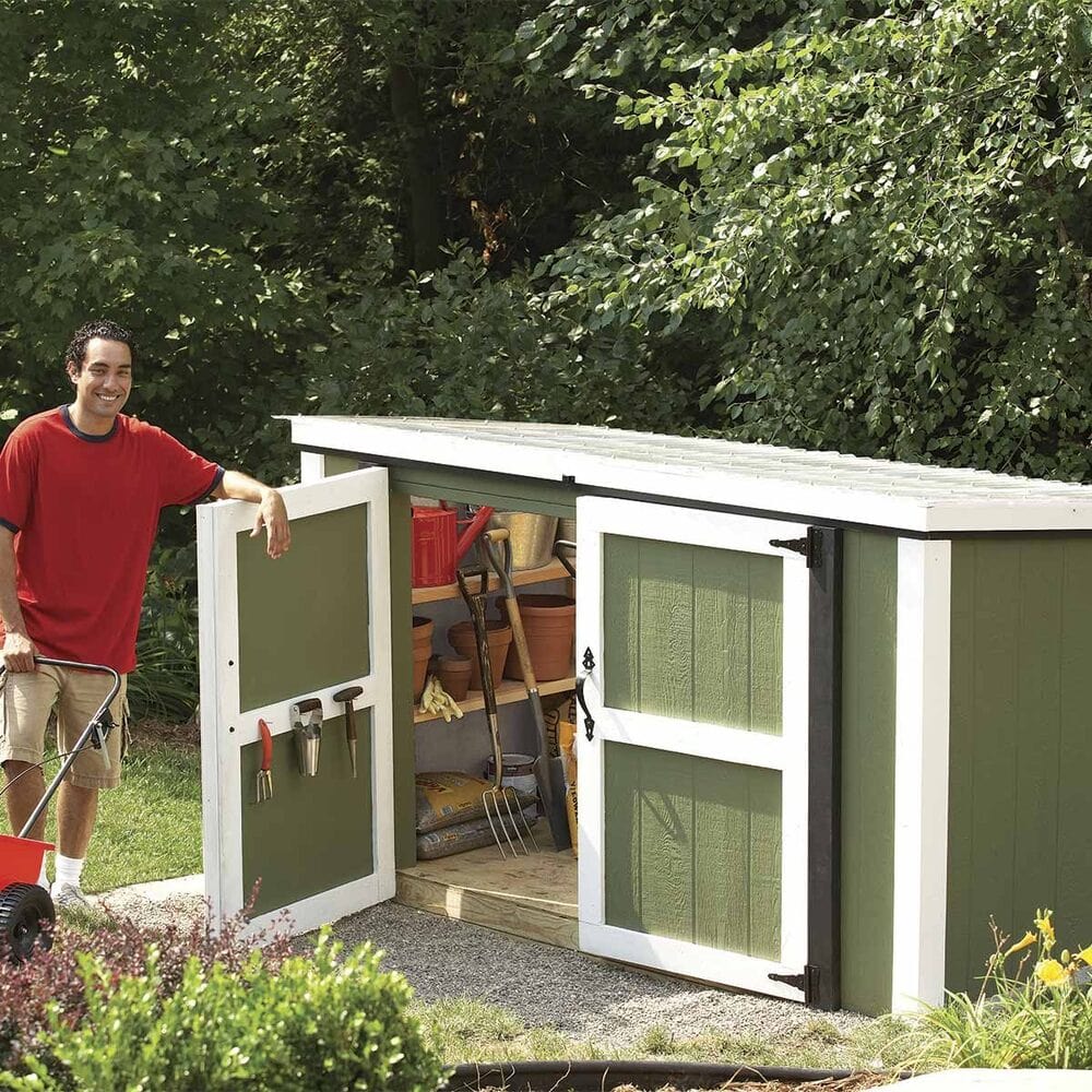 Smiling man standing next to an open green garden shed filled with tools and supplies.