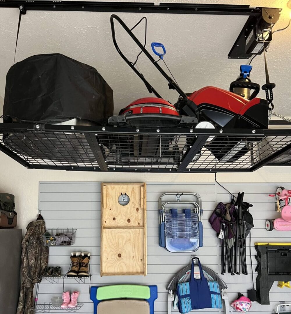Overhead storage rack in a garage holding a red lawn mower and other items, with organized gear on the wall below.