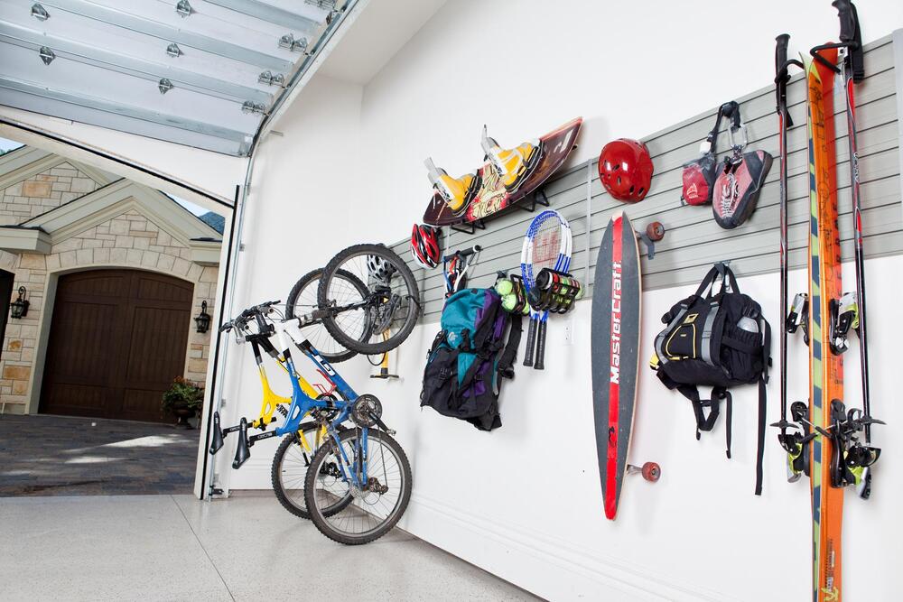 Organized garage wall with hanging bikes, skis, sports gear, and backpacks near an open door.