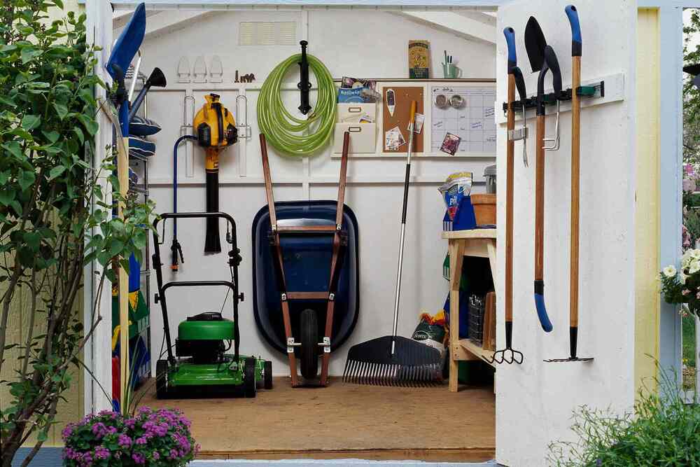  Neatly organized garden shed with tools, a green lawn mower, and a wheelbarrow inside.