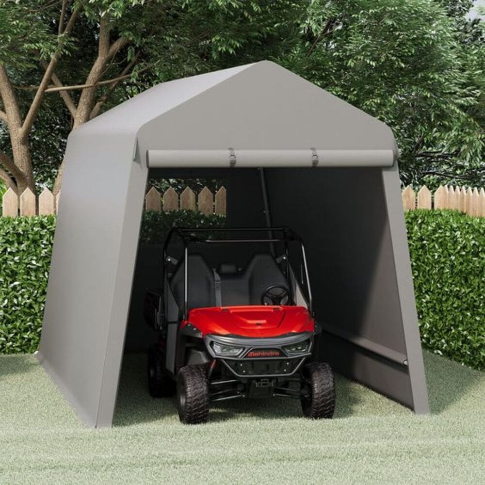 Red utility vehicle parked inside a gray portable shelter in a backyard with trees and a fence.