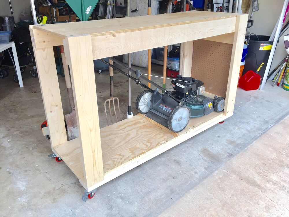 DIY wooden storage cart in a garage holding a lawn mower and garden tools.