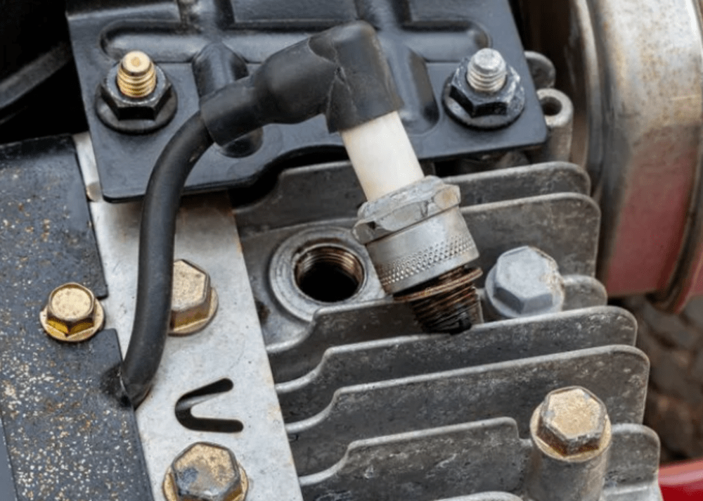 Close-up of a partially removed lawn mower spark plug with the engine exposed