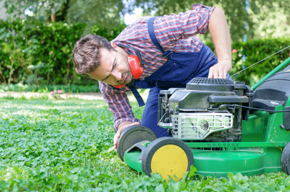 Man inspecting a green lawn mower on a lush lawn while adjusting the front wheel
