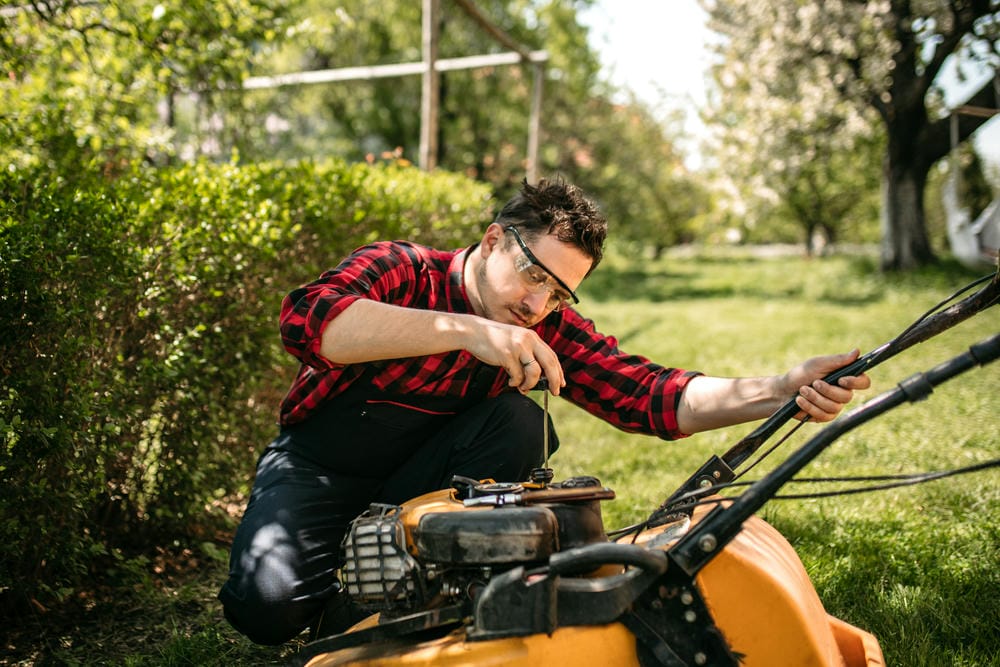 Man in safety glasses repairing a lawn mower outdoors.