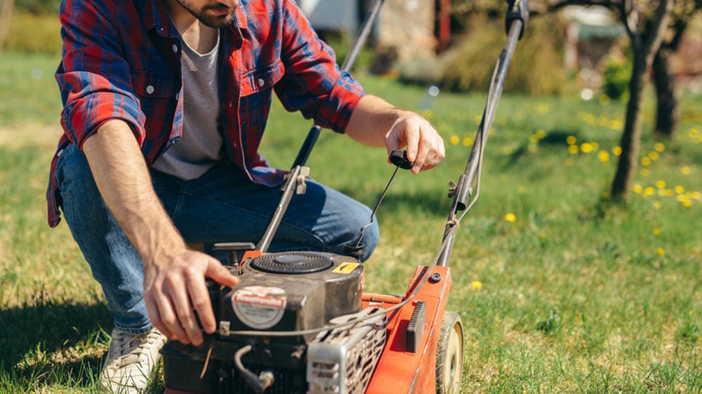 Man starting a red lawn mower by pulling the cord, preparing to mow the grass.