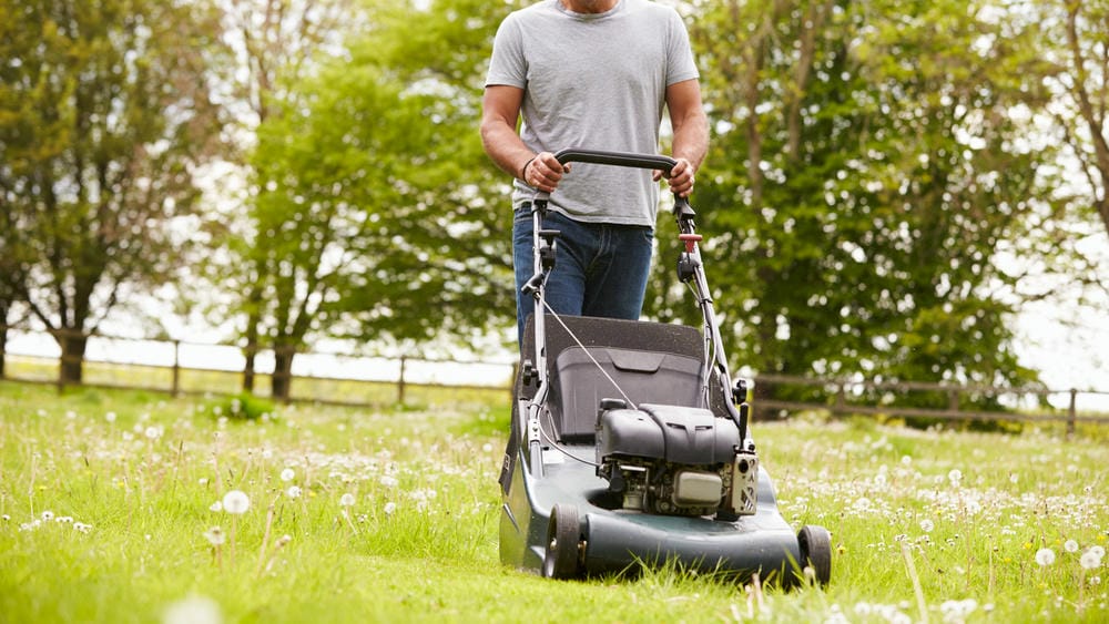 Man mowing a field with a push lawn mower in a large yard.