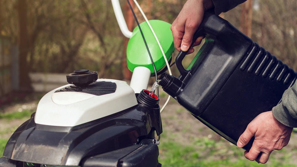 Pouring fuel from a black container into a garden trimmer