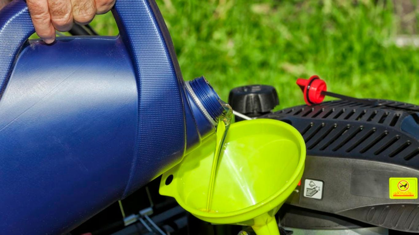 Person pouring oil into a lawn mower engine using a bright green funnel.