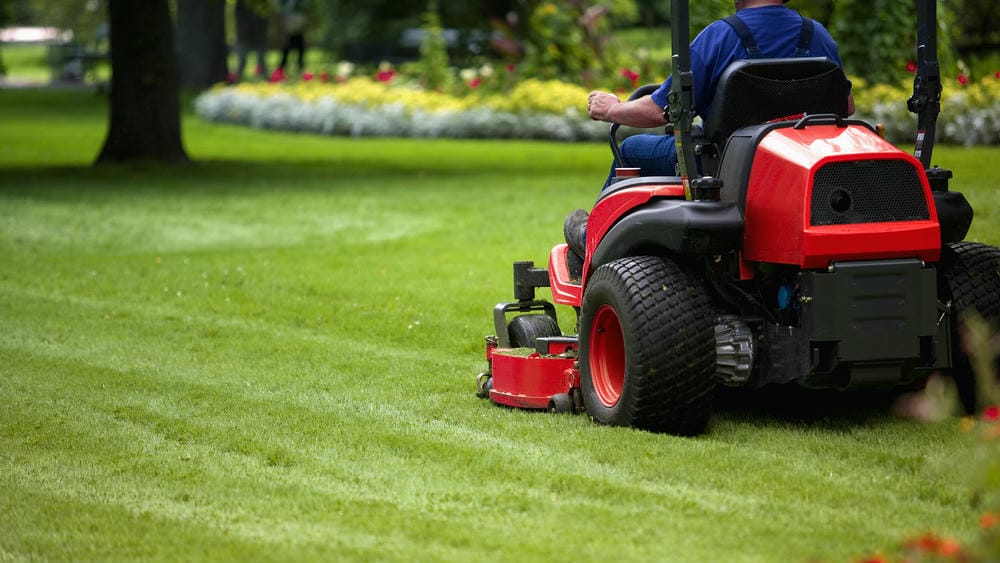 Person mowing a large lawn with a red riding lawn mower