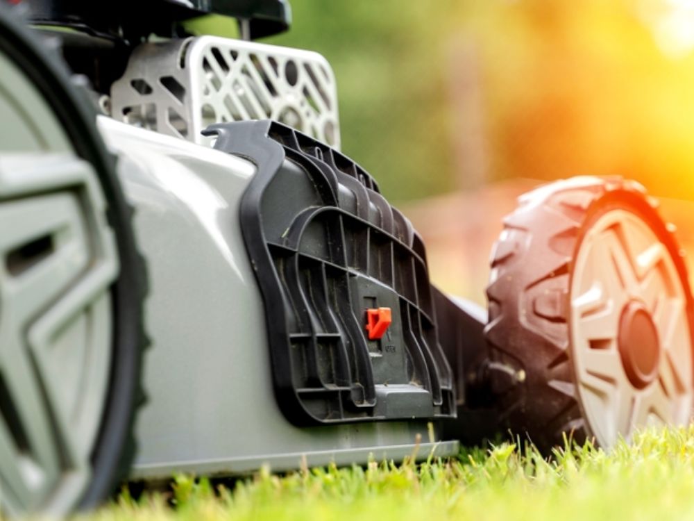 Close-up of a self-propelled lawn mower's large wheels cutting grass at sunset.