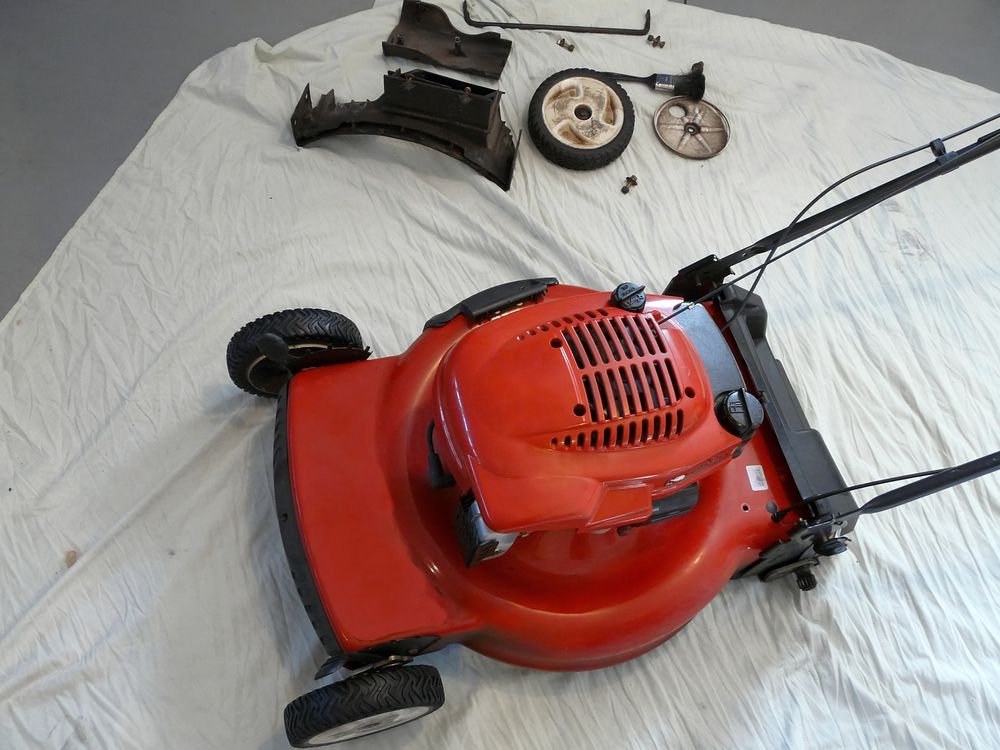 Red lawn mower undergoing maintenance with removed wheels and parts laid nearby.