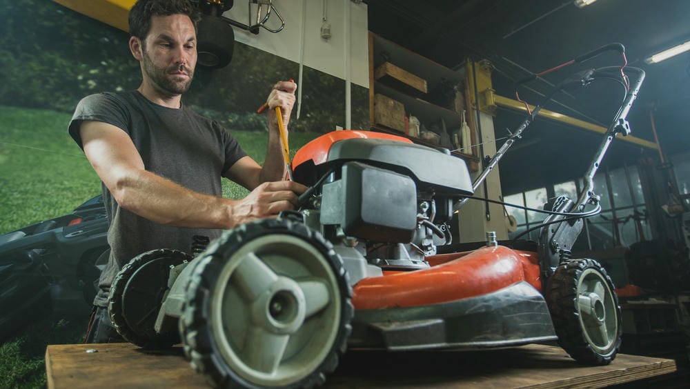 Man works on a lawn mower engine in a garage, tightening a bolt