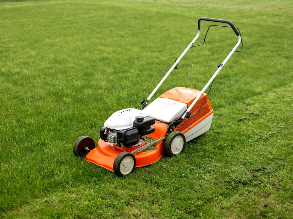 A bright orange lawn mower cuts grass in a neatly trimmed yard on a sunny day