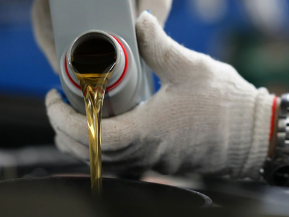 Person wearing gloves pouring oil from a bottle during maintenance.